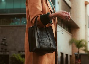 a woman wearing a brown coat and holding a black purse